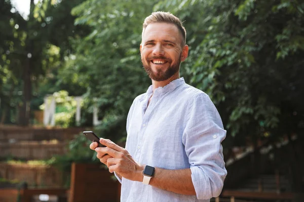 Mutlu genç sakallı adam açık havada cep telefonuyla sohbet kullanarak fotoğraf. Görünümlü kamera.