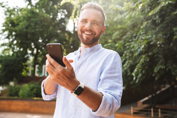 Mutlu genç sakallı adam açık havada cep telefonuyla sohbet kullanarak fotoğraf. Görünümlü kamera.