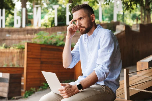 Konsantre Genç sakallı adam açık havada dizüstü bilgisayar kullanan resmi.