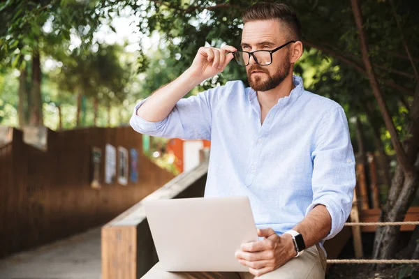 Konsantre Genç sakallı adam açık havada dizüstü bilgisayar kullanan resmi.