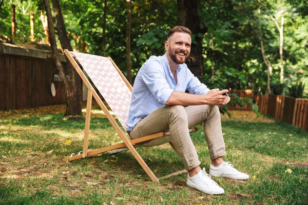 Fotoğraf gülümseyen duygusal Genç sakallı adam açık havada istimal hareket eden telefon.
