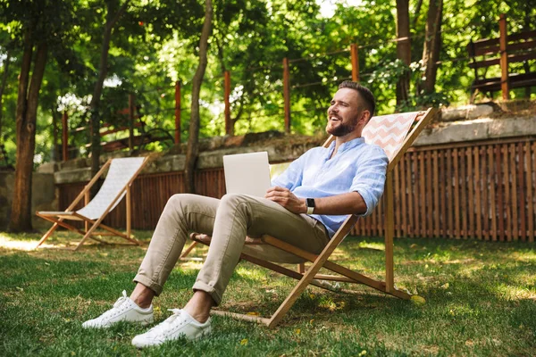 Fotoğraf gülümseyen duygusal Genç sakallı adam açık havada dizüstü bilgisayar kullanan.