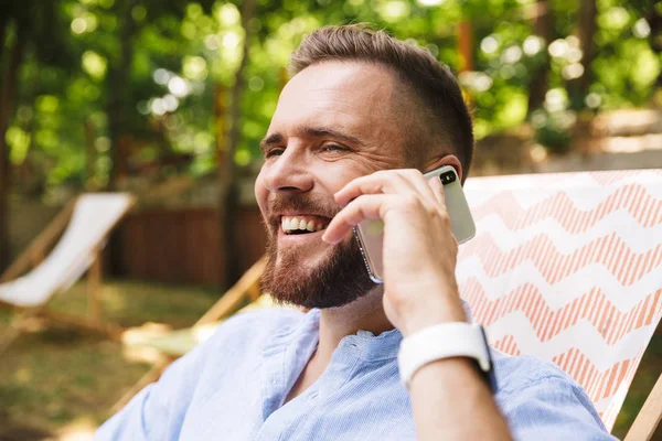 Mutlu genç sakallı adam açık havada cep telefonuyla konuşurken görüntüsünü.