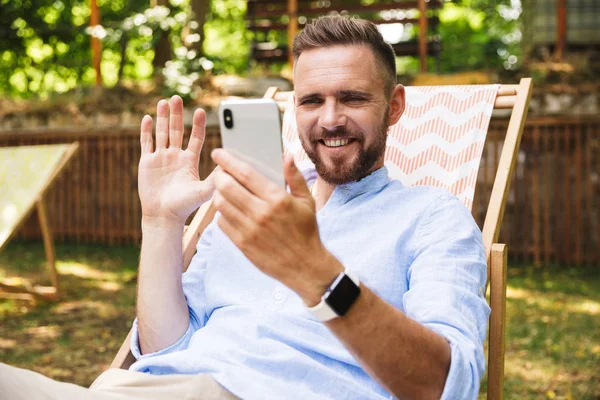 Mutlu genç sakallı adam açık havada cep telefonu sallayarak konuşuyor fotoğrafı.