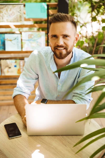 Fotoğraf gülümseyen duygusal Genç sakallı adam açık havada dizüstü bilgisayar kullanan.
