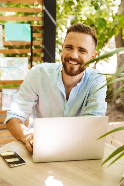 Fotoğraf gülümseyen duygusal Genç sakallı adam açık havada dizüstü bilgisayar kullanan.