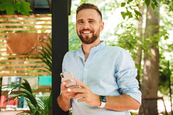 Fotoğraf gülümseyen duygusal Genç sakallı adam açık havada istimal hareket eden telefon fotoğraf makinesi arıyorum.