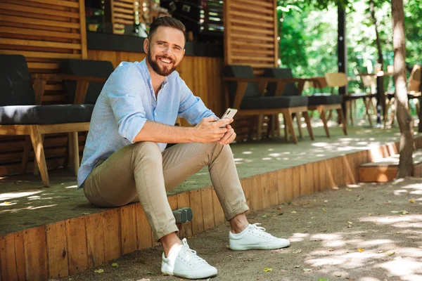 Fotoğraf gülümseyen duygusal Genç sakallı adam açık havada istimal hareket eden telefon fotoğraf makinesi arıyorum.