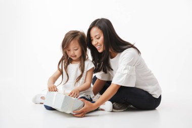 Neşeli Genç Asyalı kadın anne görüntüsünü beyaz duvar arka plan üzerinde izole oturan küçük kız çocuk kızı mevcut bir hediye kutusu sağlar.