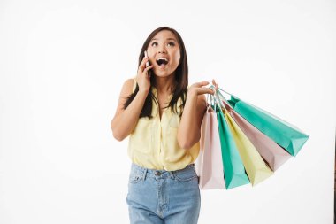 Mutlu duygusal Genç Asyalı kadın beyaz duvar arka plan üzerinde alışveriş torbaları cep telefonuyla konuşurken ile izole görüntüsünü.