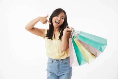 Mutlu duygusal Genç Asyalı kadın beyaz duvar arka plan üzerinde alışveriş torbaları ile işaret izole görüntüsünü.