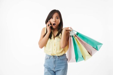 Beyaz duvar arka plan üzerinde alışveriş torbaları cep telefonuyla konuşurken ile izole şok Genç Asyalı kadın görüntüsünü.