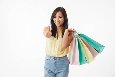 Mutlu duygusal Genç Asyalı kadın ile alışveriş torbaları jest Yaşasın gösterilen beyaz duvar arka plan üzerinde izole görüntüsünü.