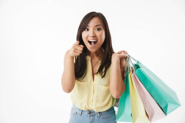 Mutlu duygusal Genç Asyalı kadın beyaz duvar arka plan üzerinde alışveriş torbaları için işaret ile izole görüntüsünü.