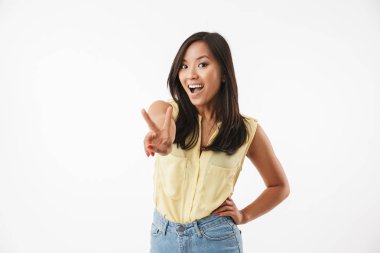 Beyaz duvar arka plan üzerinde izole mutlu Genç Asyalı kadın görüntüsü. Kamera gösteren barış hareketi arıyorsunuz.