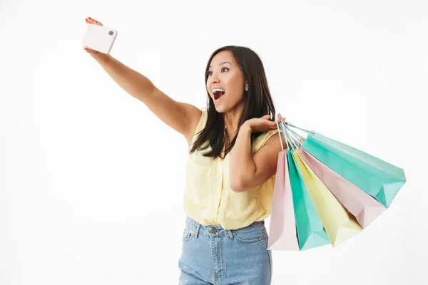 快乐情感的形象年轻的亚洲妇女被隔离在白色墙壁背景与购物袋做自拍手机 — 图库照片