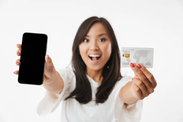 模糊照片的快乐黑发亚洲妇女穿着休闲服装显示在相机信用卡和黑色智能手机在白色背景下隔离 — 图库照片