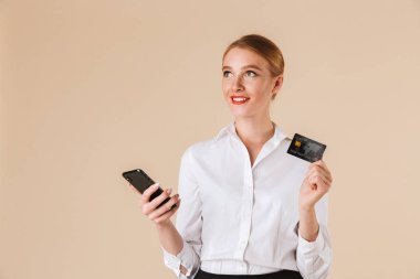 Amaç bir kenara istimal hareket eden telefon kredi kartı tutan bej duvar bakmaktan izole duran genç iş kadını görüntüsünü.