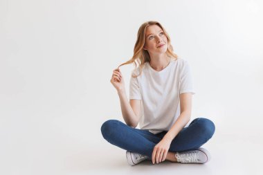 Beyaz duvar arka plan üzerinde izole oturan güzel genç şirin kızıl saçlı kadın resmi. Bir kenara arıyorsunuz.