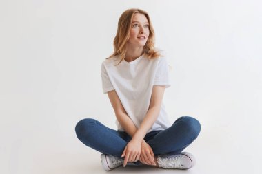 Beyaz duvar arka plan üzerinde izole oturan güzel genç şirin kızıl saçlı kadın resmi. Bir kenara arıyorsunuz.