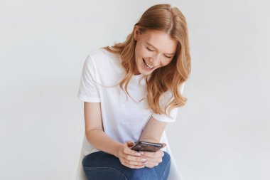 Cep telefonu kullaranarak beyaz duvar arka plan üzerinde izole genç redhead mutlu kadın görüntüsünü.