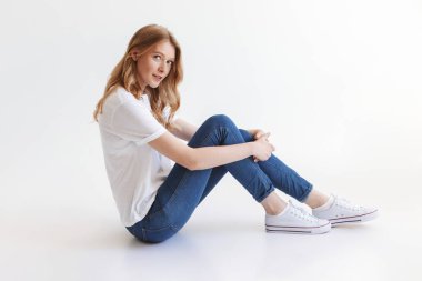 Görüntü izole kamera seyir beyaz duvar arka plan üzerinde oturan genç güzel kızıl saçlı kadın.