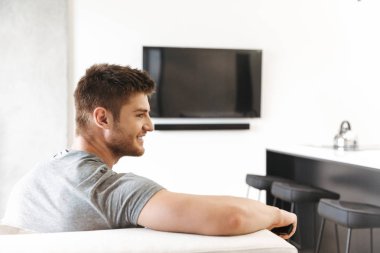 Arkadan görünüşü Tv Uzaktan kumanda ile evde bir kanepede oturan gülümseyen genç adam