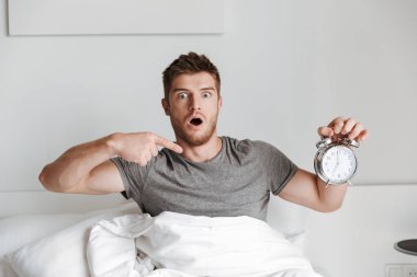 Evde yatakta otururken şok genç adam gösteren çalar saat