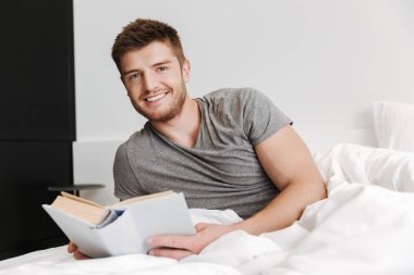 Mutlu genç adam evde yatakta döşeme sırasında bir kitap okuma