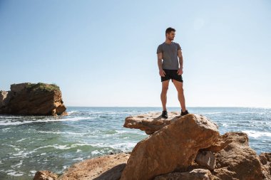 Deniz kıyısı bir kayanın üzerinde ayakta ve uzak arıyorum genç sporcu