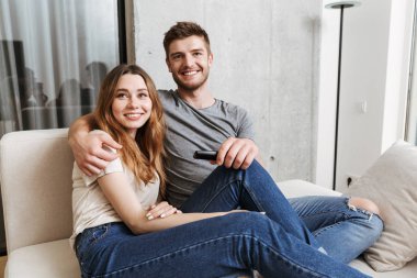 Genç çift birlikte evde bir kanepede oturan ve Tv izlerken sarılma gülümseyen