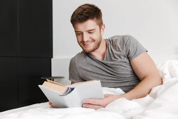 Усміхнений Молодий Чоловік Читає Книгу Ліжку Вдома — стокове фото