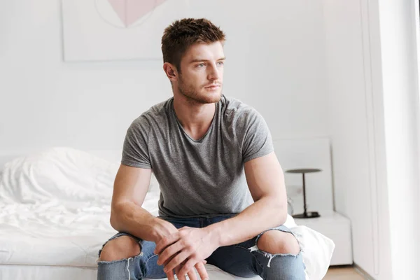Konzentrierter Junger Mann Sitzt Hause Auf Seinem Bett Und Schaut — Stockfoto