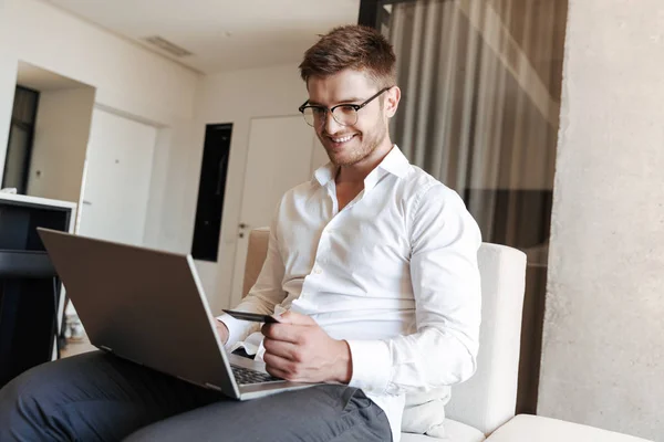 Pria Muda Tersenyum Memegang Kartu Kredit Saat Menggunakan Komputer Laptop — Stok Foto