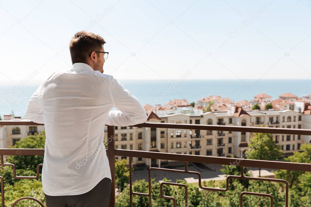 Back view of a young man standing on a balcony looking at a beautiful cityscape