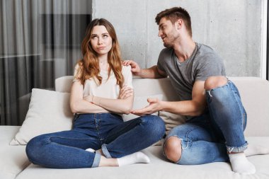 Evde bir kanepede oturan üzgün kız arkadaşına konuşmaya çalışan adam