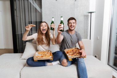 Pizza yiyip birlikte evde kanepede oturan ve Tv izlerken bira içmeyi genç çift