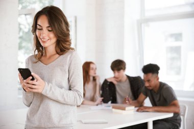 Görüntü gülümseyen genç kadının kapalı birbirleri ile bir şey yazma konuşmak sınıfta arkadaş öğrencileri ise cep telefonu kullanarak.