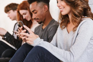 Görüntü kapalı cep telefonunu kullanarak beyaz duvar artalan üzerinde oturan genç arkadaşlar öğrenci. Neşeli kadın odaklanmak.