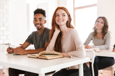 Mutlu kızıl Bayan öğrenci sınıf kapalı bir kenara arıyorum Afrika arkadaş adam yakın oturan görüntüsünü.