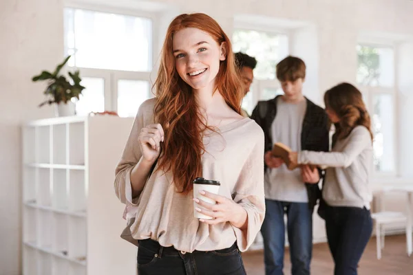 屋内でお互い話して教室で立っている若い幸せな友人学生のイメージ コーヒーを飲みながら幸せな赤毛の女性に焦点を当てる — ストック写真