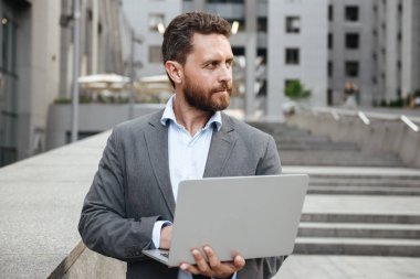 Beyaz ofis insanın 40s klasik görüntü uygun büyük şehirde iş merkezi önünde dururken açık gümüş dizüstü holding