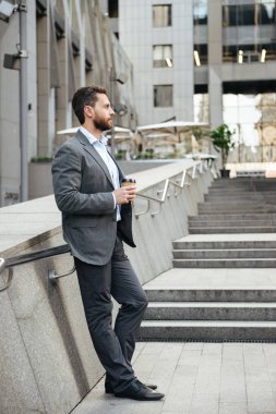 Tam uzunlukta profil resmi emin iş adamı 40'lı gri takım elbise modern iş merkezi önünde ayakta ve içme paket servisi olan restoran kahve