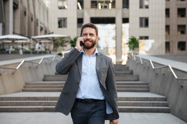Mutlu iş adamı 40'lı modern iş merkezi dışında merdivenlerden aşağı yürürken cep telefonu konuşma gri elbiseli portre closeup