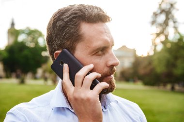 Beyaz gömlek arıyorum ciddi adam 40'lı bir kenara siyah Smartphone'da konuşurken yeşil parkta yürüyüş sırasında portre closeup