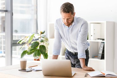 Dizüstü bilgisayar süre ayakta ve ofiste bir masa üzerine eğilerek arayan yoğun iş adamı