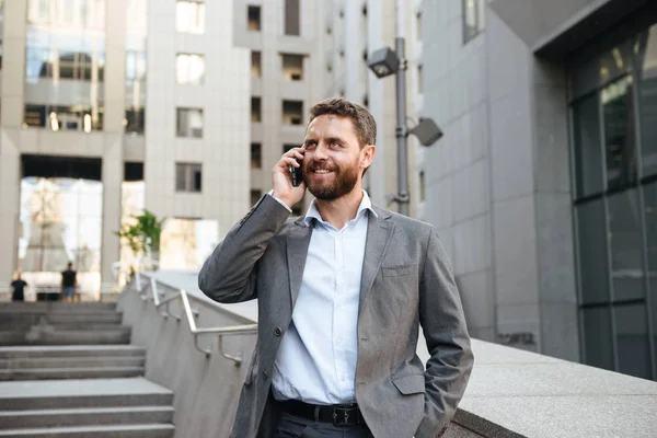 Gri takım konuşan neşeli iş adamı 40'lı cep telefonunda modern iş merkezi dışında merdivenlerden aşağı yürürken gülümseyen bir portre portre