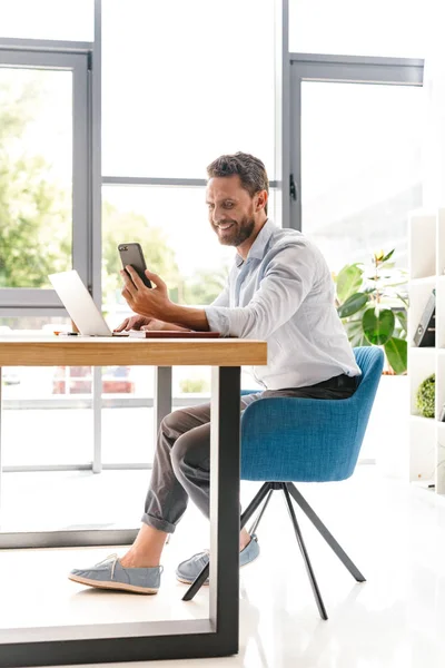 Imagem Homem Barbudo Bonito Feliz Sentado Escritório Trabalhando Olhando Para — Fotografia de Stock