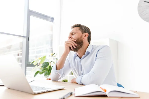 Foto Van Moe Geeuwen Bebaarde Man Zit Office Laptopcomputer Werkt — Stockfoto