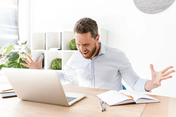 stock image Photo of agressive bearded man sitting in office working on laptop computer. Looking aside.